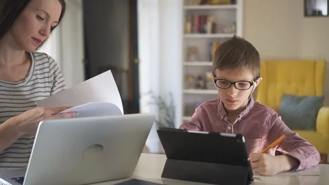 Modern mom is using a laptop check documents working and kid doing homework with Stock Footage 129532639