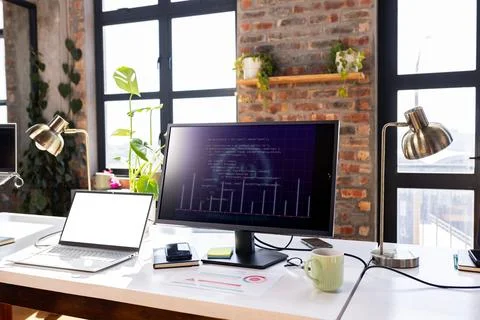 Modern office desk with computer screen displaying coding project and laptop. Stock Photos