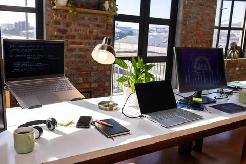 Modern office desk with laptops, coding on screens, and coffee mug. Technolog 스톡 사진