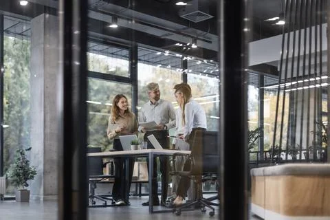 A modern office interior, featuring a blurred view of workers at desks, throu Stock Photos
