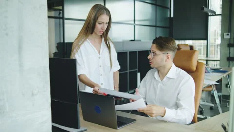 In a modern office, a man sits at his computer looking troubled as a female Stock Footage 326703833