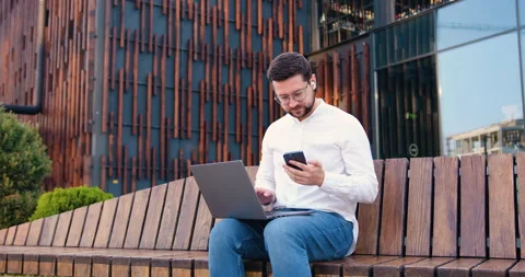 Modern office worker in casual clothes using laptop and phone while sitting on Stock Footage 316310579