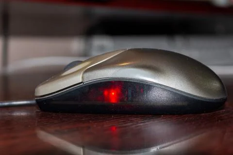 Modern optical computer mouse with red light sensor on dark wooden desk surface Stock Photos