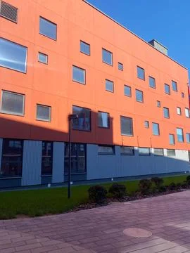 Modern orange building facade with multiple windows and green grass in front Stock Photos