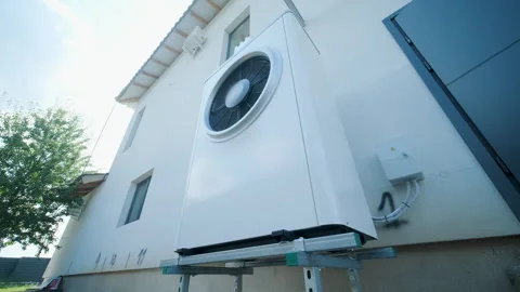 Modern outdoor air-source heat pump unit with a large fan on a white residential Stock Footage 340112904
