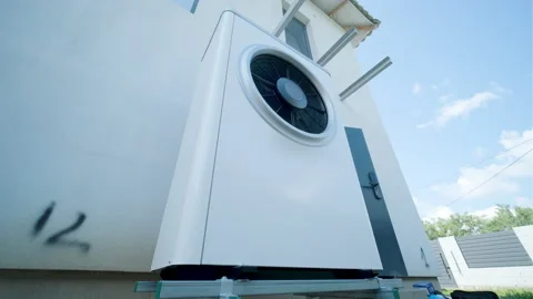 Modern outdoor air-source heat pump unit with a large fan on a white residential Stock Footage 340112907