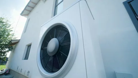 Modern outdoor air-source heat pump unit with a large fan on a white residential Stock Footage 340112919
