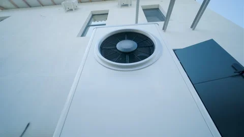 Modern outdoor air-source heat pump unit with a large fan on a white residential Stock Footage 340112922