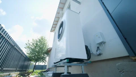 Modern outdoor air-source heat pump unit with a large fan on a white residential Stock Footage 340112933