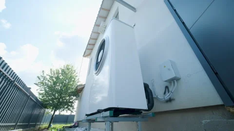 Modern outdoor air-source heat pump unit with a large fan on a white residential Stock Footage 340112934