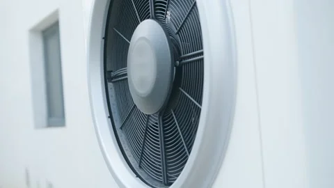 Modern outdoor air-source heat pump unit with a large fan on a white residential Stock Footage 340112968