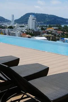 Modern outdoor infinity pool with three lounge chairs overlooking a cityscape Stock Photos