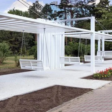 A modern outdoor space featuring white swings under a minimalist structure... Stock Photos