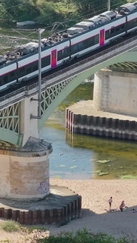 A modern passenger train crossing a metal railway bridge over the Loire River in Stock Footage 346662702