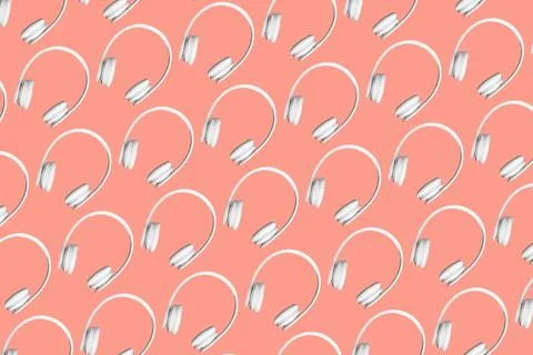 Modern pattern of white wireless headphones on peach coloured background. Stock Photos