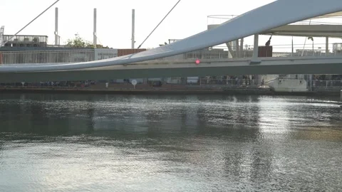 Modern pedestrian bridge over tranquil river with industrial background at sunse Stock Footage 315737666