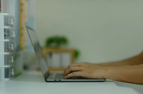 Modern person typing on laptop computer at work desk in home office setting Stock Photos