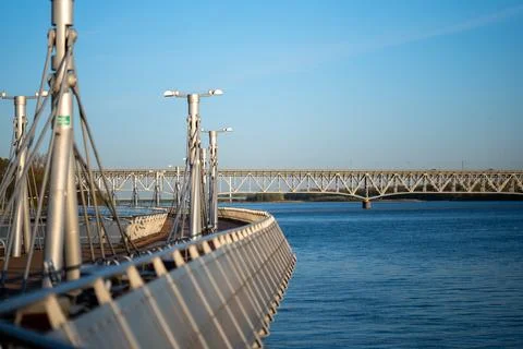 Modern pier with original lanterns overlooking a large steel bridge and a river Фото