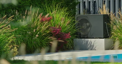 Modern pool heat pump unit placed near garden plants and grasses, next to Stock Footage 308940646