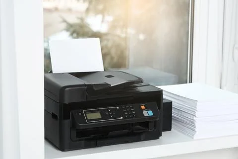 Modern printer and stack of paper on window sill indoors Foto stock