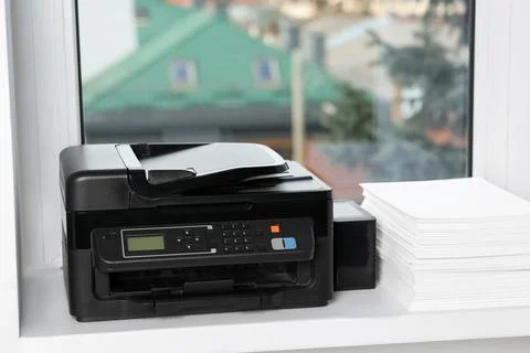 Modern printer and stack of paper on window sill indoors 库存照片