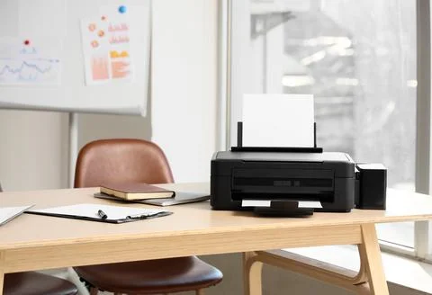 Modern printer on desk near window in office Stock Photos