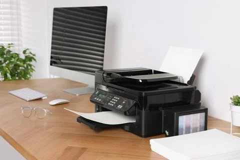 Modern printer with paper near computer on wooden table in office Stock Photos
