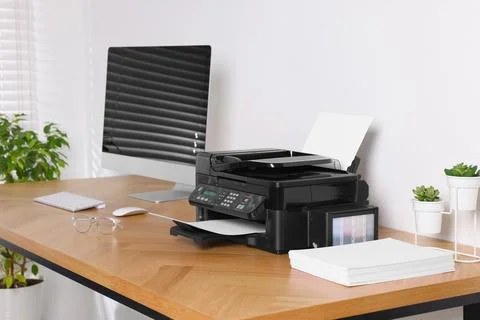 Modern printer with paper near computer on wooden table in office Stock Photos