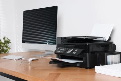 Modern printer with paper near computer on wooden table in office Stock Photos