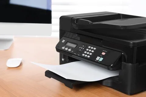 Modern printer with paper near computer on wooden table in office Stock Photos