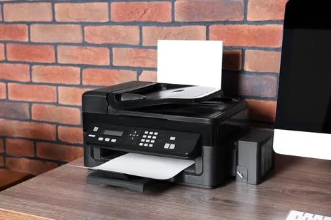 Modern printer with paper near computer on wooden desk at home Stock Photos