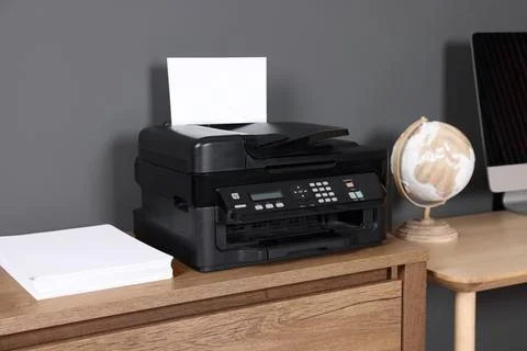 Modern printer with paper near computer on wooden desk at home Stock Photos