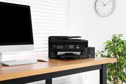 Modern printer with paper near computer on wooden table in home office Stock Photos