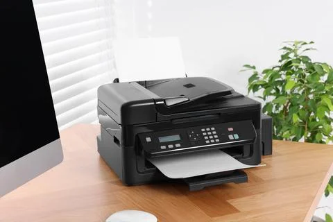 Modern printer with paper near computer on wooden table in home office Stock Photos