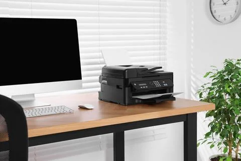Modern printer with paper near computer on wooden table in home office Stock Photos