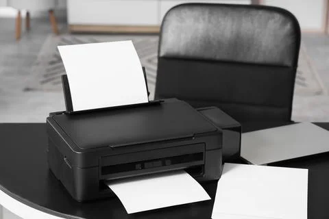 Modern printer with paper sheets and laptop on desk in office Stock Photos