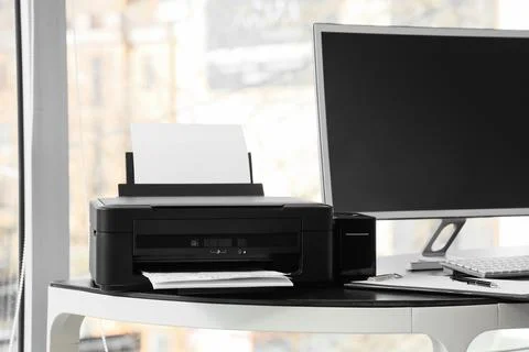 Modern printer with paper sheets and computer on desk in office Stock Photos