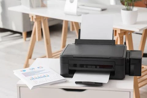 Modern printer with paper sheets on chest of drawers in office Stock Photos