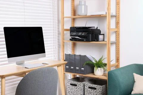 Modern printer on shelf near table with computer in home office Stock Photos