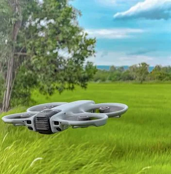 Modern Quadcopter Drone Hovering Above Green Agricultural Field with Blue Sky Stock Photos