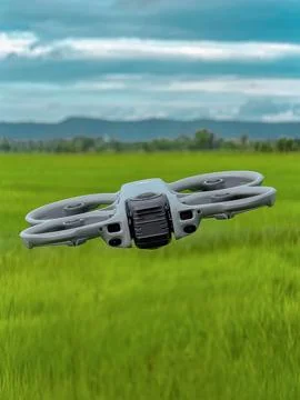 Modern Quadcopter Drone Hovering Above Green Agricultural Field with Blue Sky Stock Photos