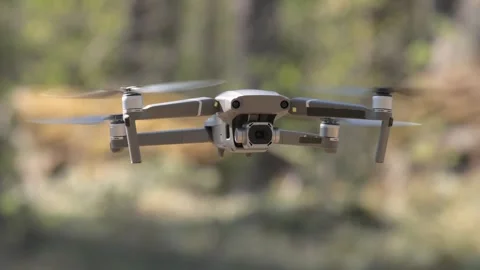 Modern quadcopter drone hovering in sunny forest setting with spinning rotors Stock Footage 337358534