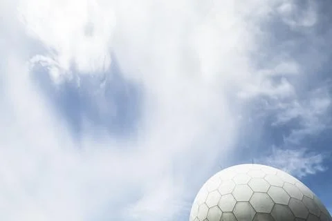 A modern radar dome structure set against a vivid blue sky with clouds Stock Photos