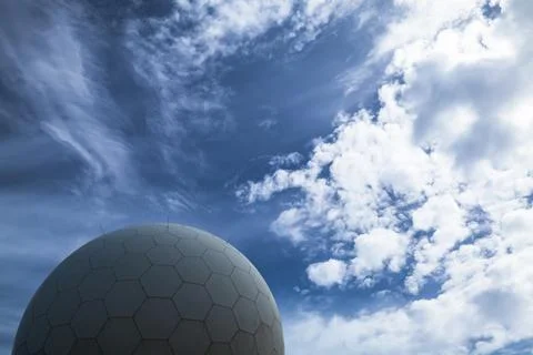 A modern radar spherical structure set against a vivid blue sky with clouds Stock Photos