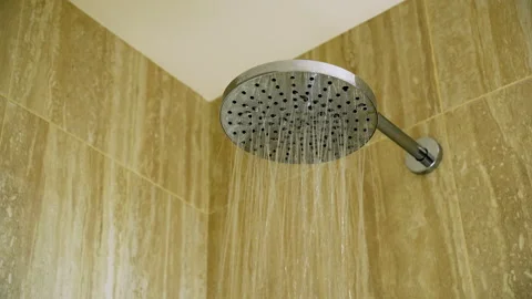 Modern rainfall shower head with running water against beige bathroom wall Stock Footage 291412540