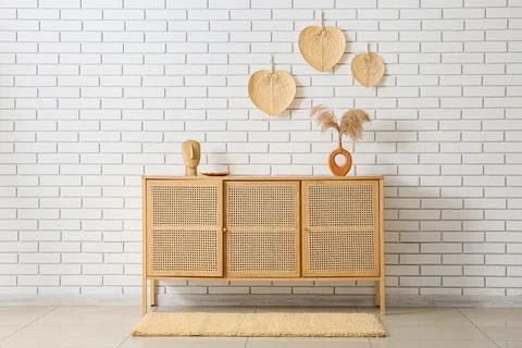 Modern rattan cabinet with decorative elements against white brick wall, mini Stock Photos