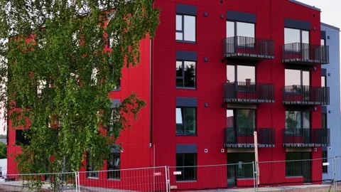 Modern red apartment building under construction with a green tree and balconies Stock Footage 341743043