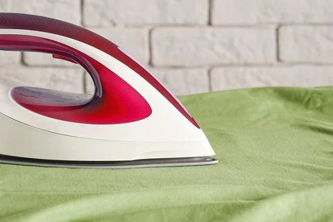 Modern red iron on the board ironing a green shirt - closeup view Stock Photos