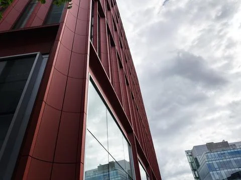 Modern red office building with reflective glass under dramatic cloudy sky .. Stock Photos