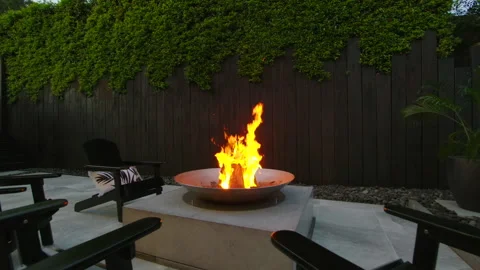 Modern roaring fire pit surrounded by chairs shot at dusk. Stock Footage 180478262
